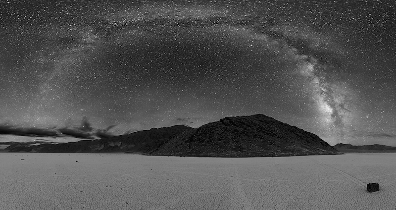 Part of a panorama of the playa of Death Valley at night. The Milky way is visible as an arc across the sky.