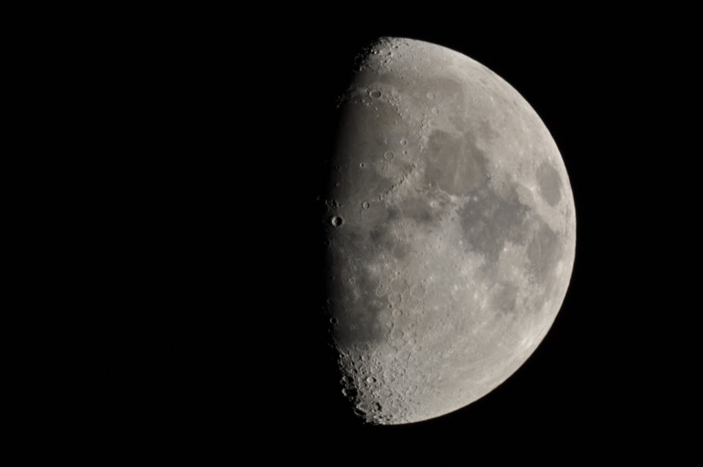 A moon where the left part is in shadow, and a little bit more than half is illuminated on the right.
