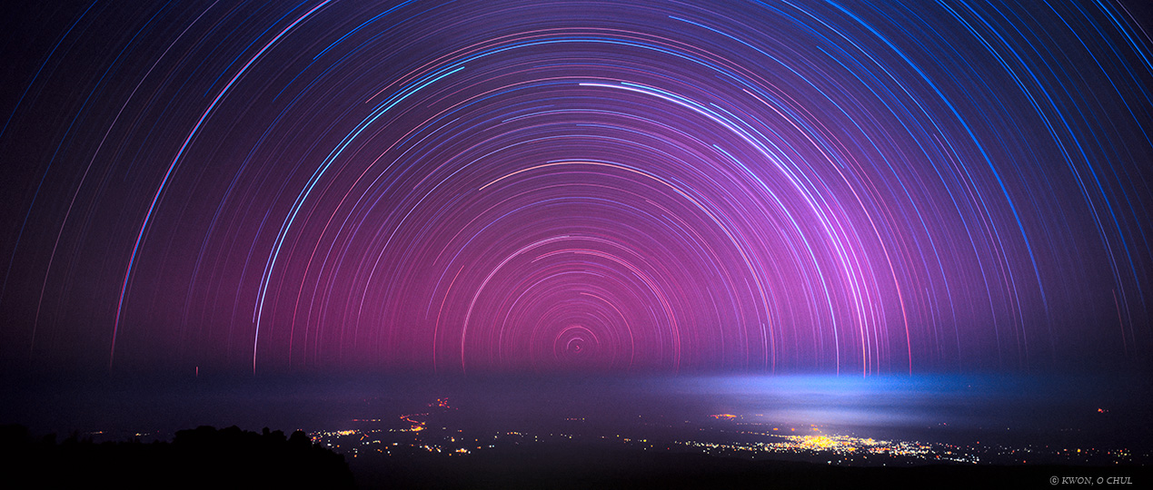 An image of star trails arcing around the south celestial pole which is close to the horizon.