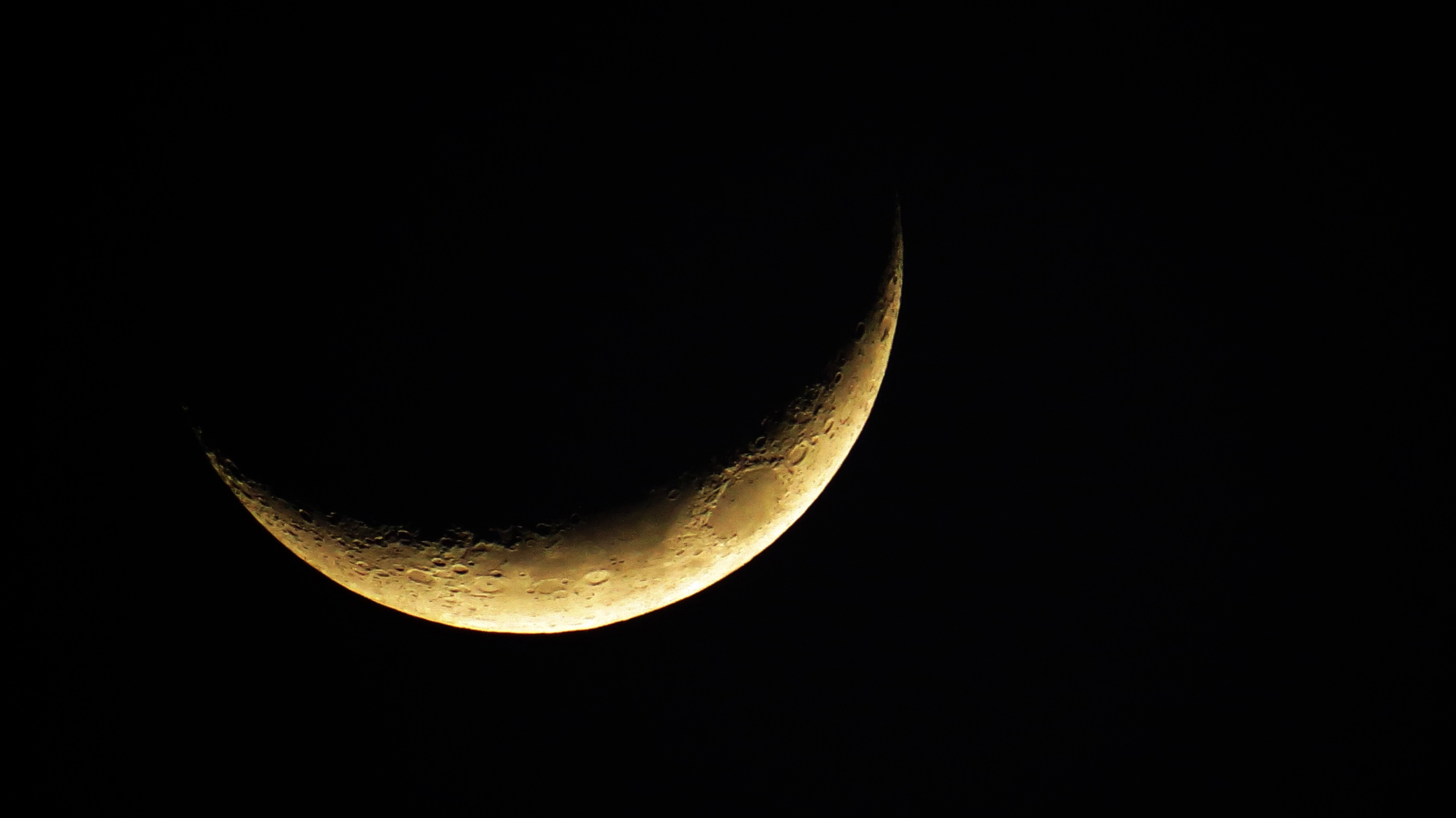 A moon with a narrow crescent illuminated on the bottom, but most in darkness.